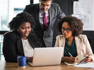 three people in a business setting looking at a laptop together